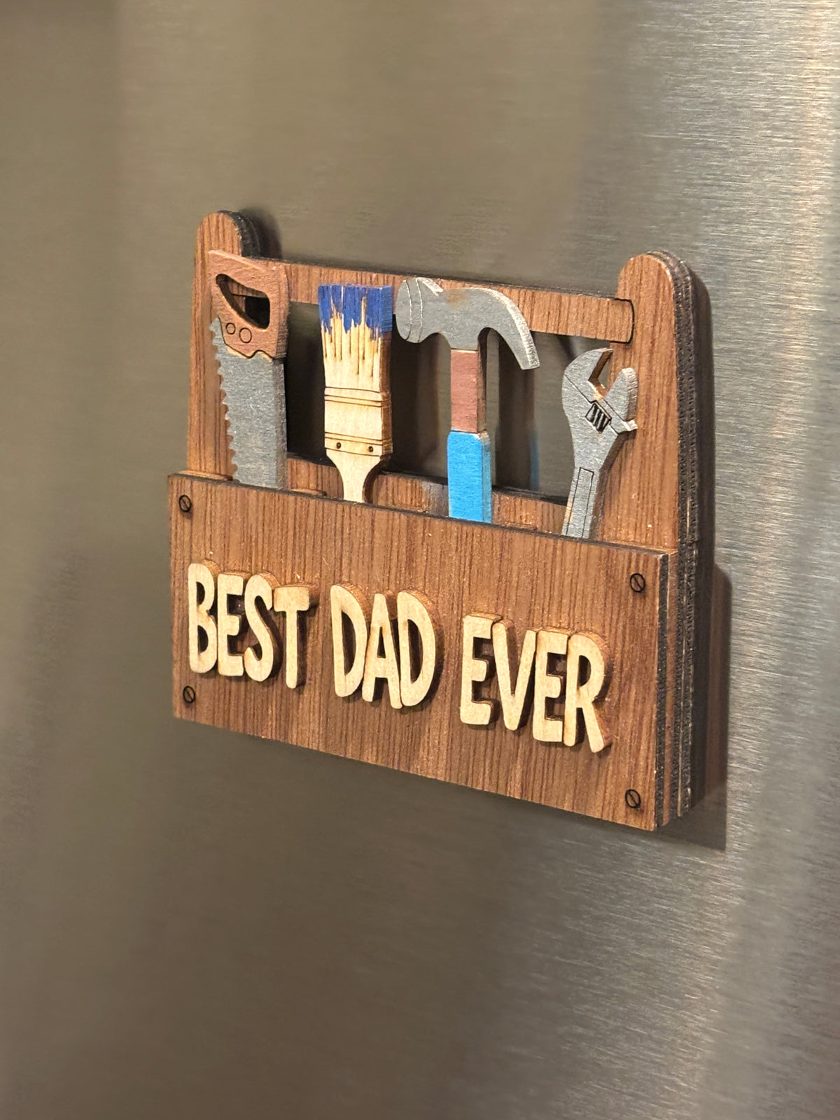 This is a side view of the "Best Dad Ever" toolbox.
This item is shown here on a refrigerator it has 2 Strong Magnets and a Hanger on the back. It also comes with a perfectly sized easel.  
 3d Unique design, Handcrafted, this item is not printed. Its laser engraved and precision cut. 
The tools are removable and can be replaced in any slot you wish.

this item measures approximately 3.5" X 4.0 inches.


