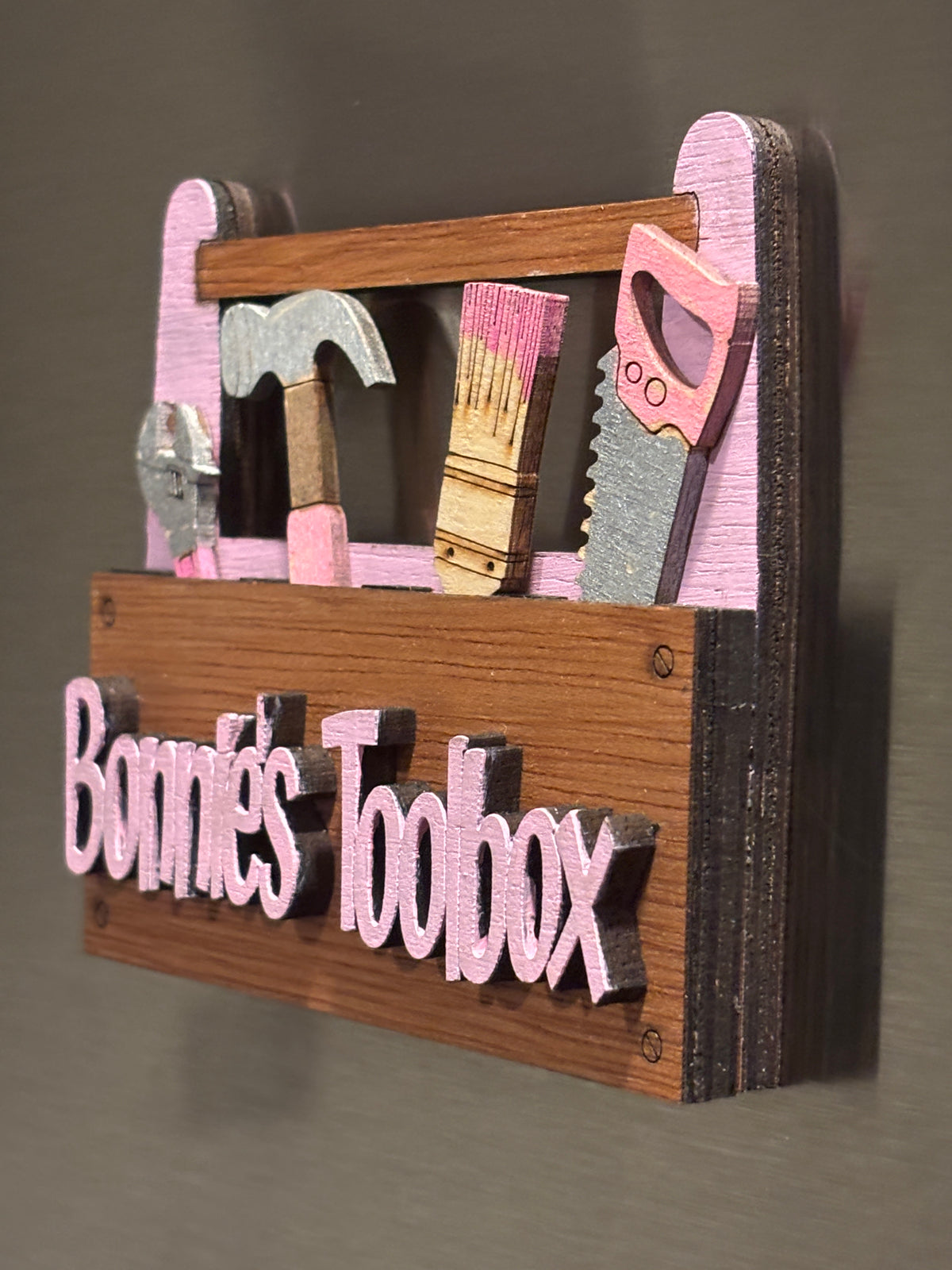 This is a side view of the "Best Dad Ever" toolbox.
This item is shown here on a refrigerator it has 2 Strong Magnets and a Hanger on the back. It also comes with a perfectly sized easel.  
 3d Unique design, Handcrafted, this item is not printed. Its laser engraved and precision cut. 
The tools are removable and can be replaced in any slot you wish.

this item measures approximately 3.5" X 4.0 inches.